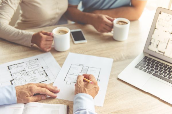 Cropped image of realtor and happy young couple discussing new house. Couple is drinking coffee while sitting in office